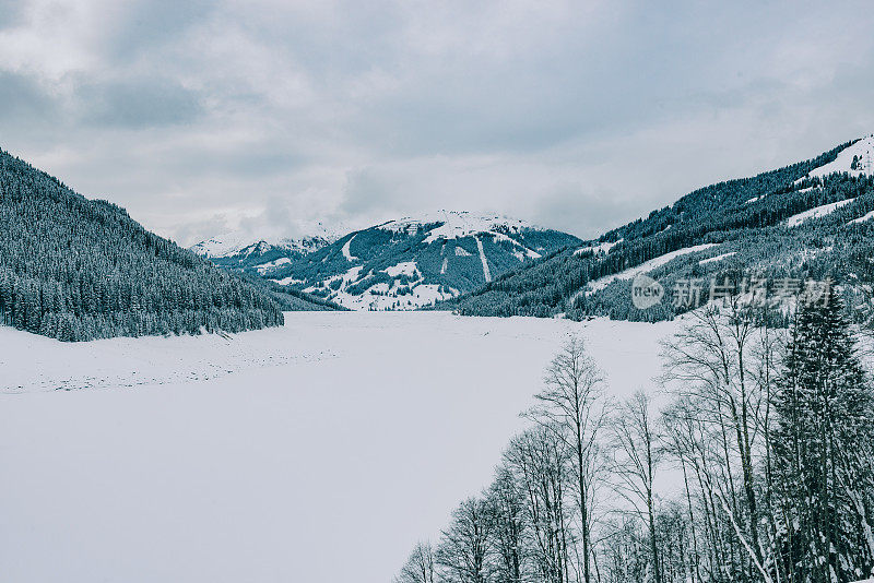 在白雪覆盖和冰冻的Speicher Durlassboden湖与松树和白雪覆盖的山脉